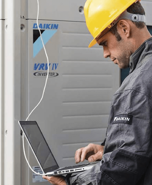Man stood next to VRF air conditioning system with laptop