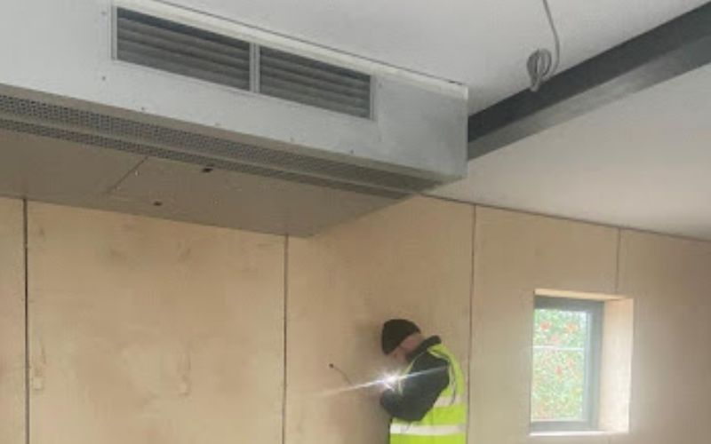 Man testing large air conditioning unit in wooden building